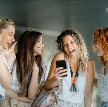four laughing female friends looking at a smartphone