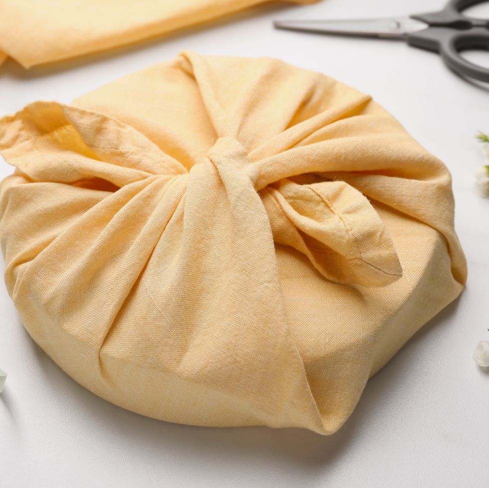 furoshiki. things packed in fabric, scissors, ribbon and flowers on white table, closeup