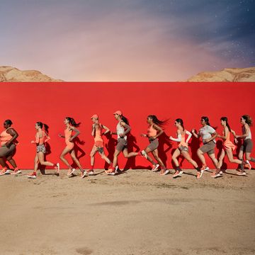 a group of people running on a dirt road with a red wall behind them