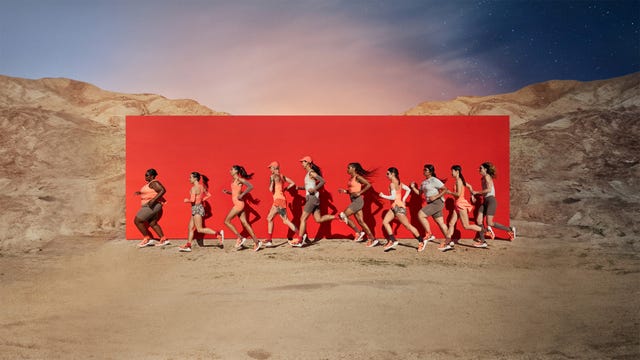 a group of people running on a dirt road with a red wall behind them