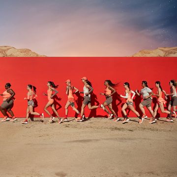 a group of people running on a dirt road with a red wall behind them