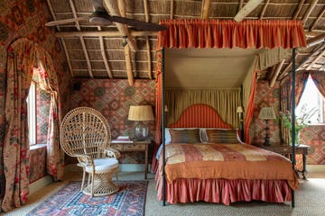 a canopy bedroom with a bed and a wicker chair and patterened walls in an orange and red tone