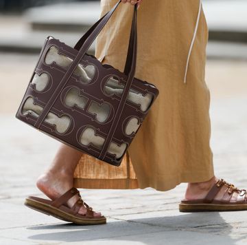 a woman wearing a tan linen maxi skirt while carrying a brown leather cutout celine tote bag with beige linen lining in a roundup of the best summer tote bags 2024