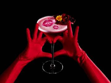 a cocktail held between gloved hands against a dark background