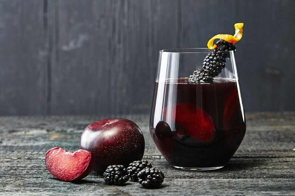 a glass of blackberry punch with blackberry garnish on a dark table