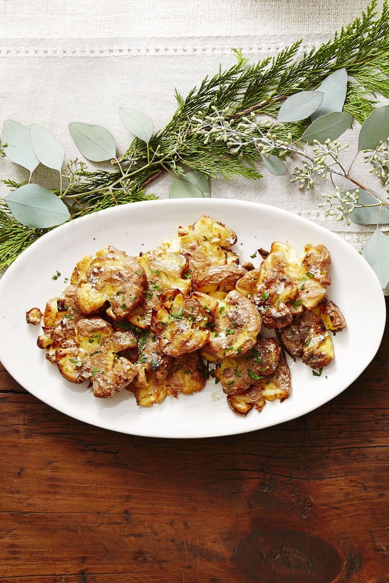 white plate of crispy golden smashed potatoes and fresh herbs