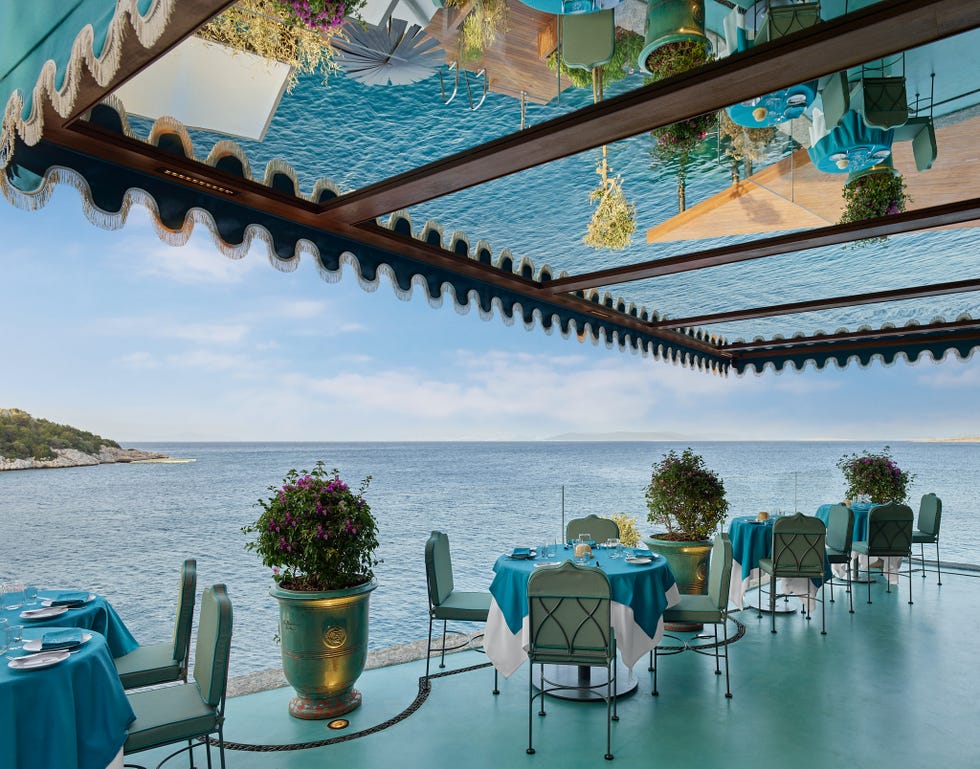 a patio with tables and chairs and a body of water in the background