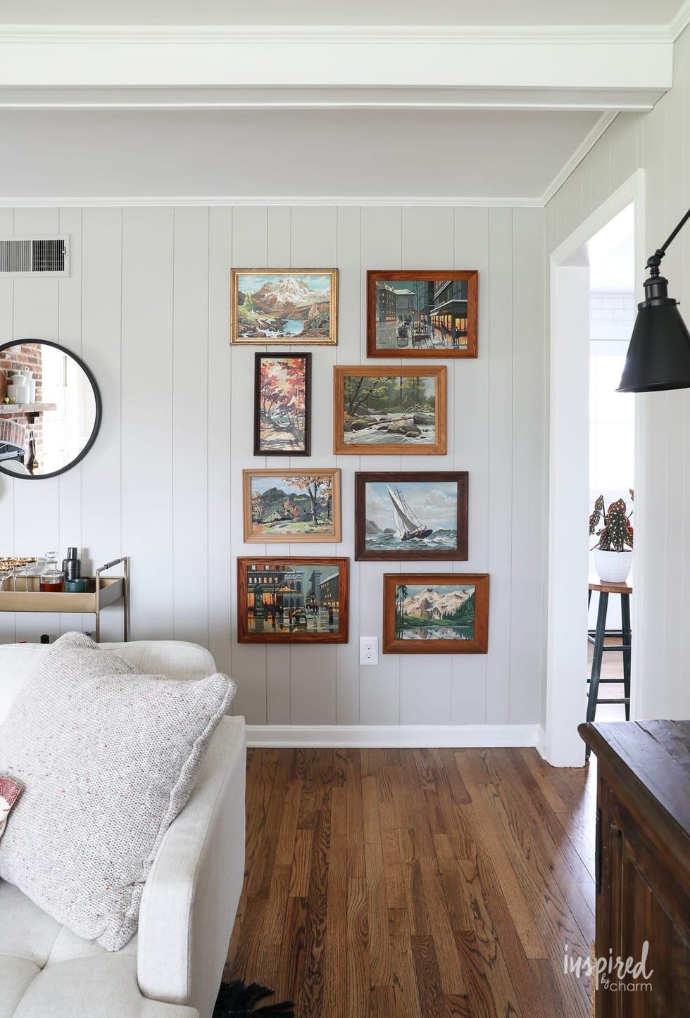 vintage art gallery wall in a room with gray wood paneling and hardwood floors