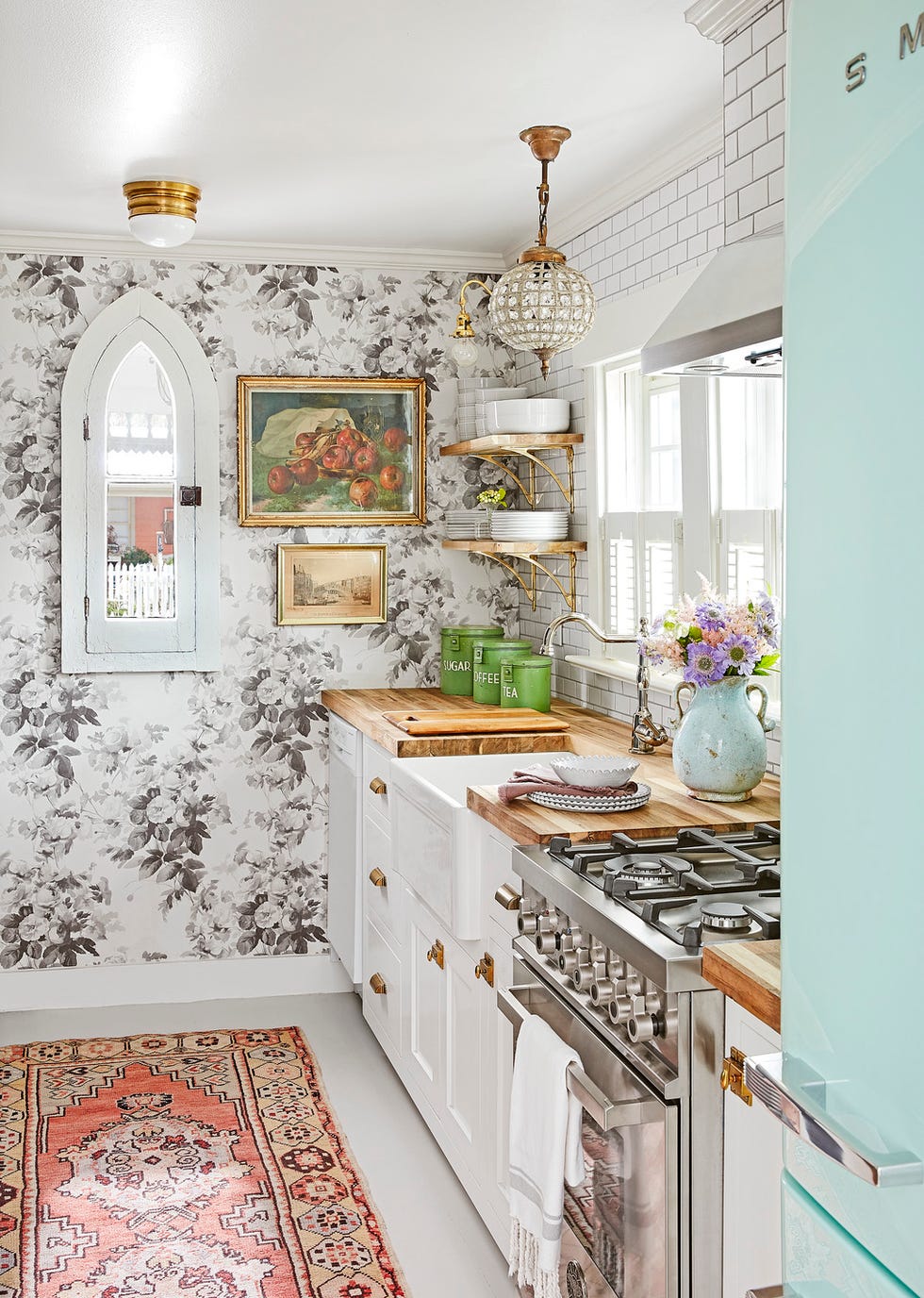 White galley kitchen with teal refrigerator, floral wallpaper and butcher block countertops