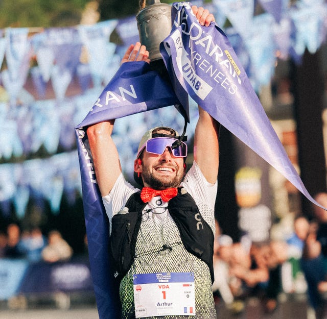 A triumphant athlete celebrating a victory while holding a trophy and banners