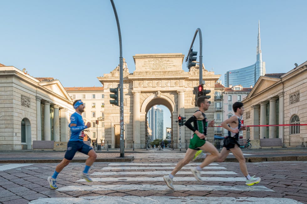 Runners in a city street with an archway in the background