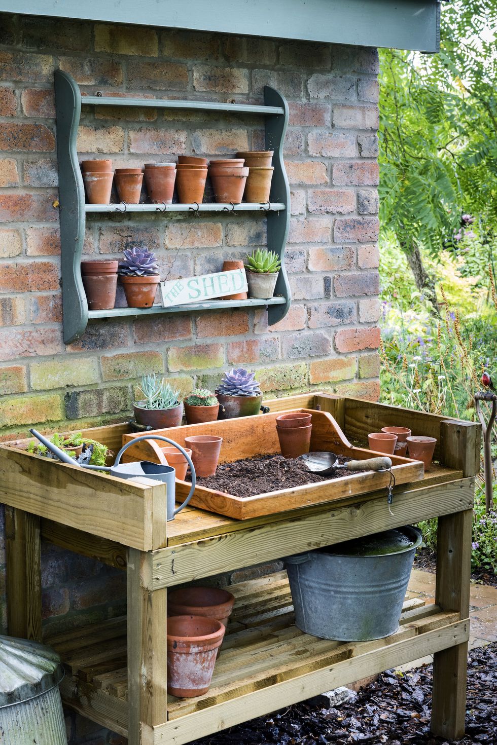 storage outer wall of potting shed with potting area, terracotta pots and pots of succulentsinclude a lower shelf for storage, plus others on walls above for little pots