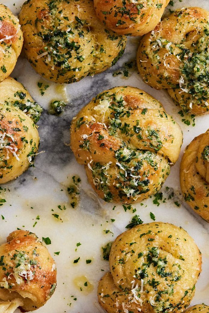 close up of garlic knots topped with parsley and parmesan on a marble background