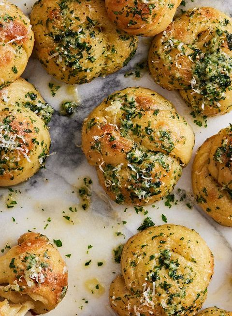 close up of garlic knots topped with parsley and parmesan on a marble background
