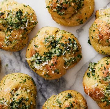 closeup of garlic knots topped with parsley, cheese, and garlic on a white marble background