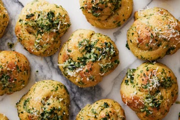 closeup of garlic knots topped with parsley, cheese, and garlic on a white marble background