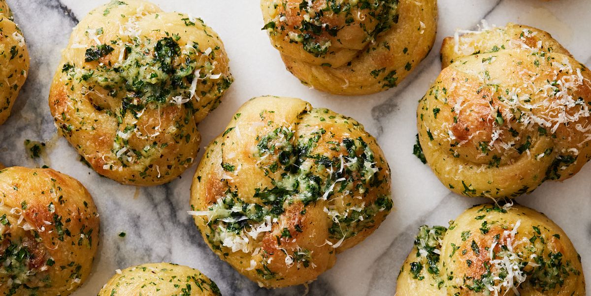 closeup of garlic knots topped with parsley, cheese, and garlic on a white marble background