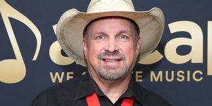 garth brooks smiles at the camera, he wears a straw cowboy hat, black collared shirt and a gold medal with a ribbon lanyard