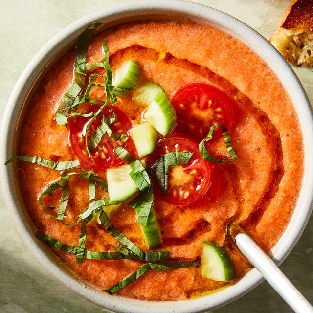 tomato gazpacho in a bowl topped with chopped cucumbers, basil, sliced cherry tomatoes, and an olive oil drizzle
