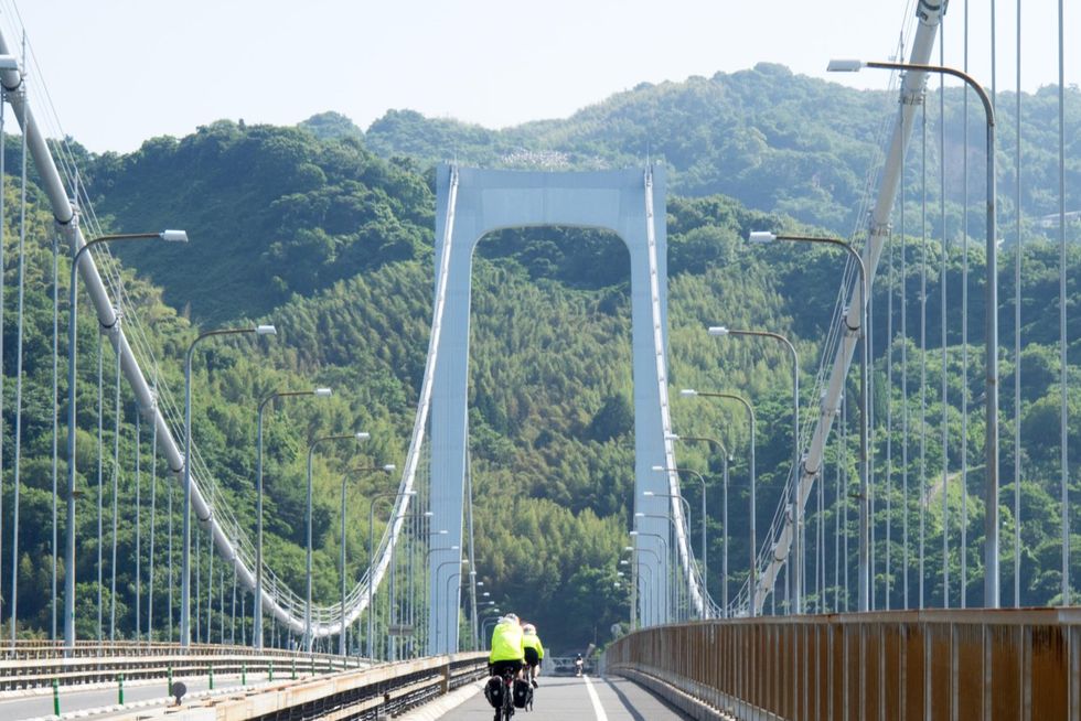 gbx92y two cyclists crossing the hakata oshima bridge connecting the islands of oshima and hakata in the seto inland sea