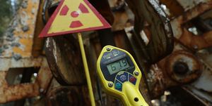 yellow digital geiger counter in the foreground with rusty metal and a nuclear warning sign in the background