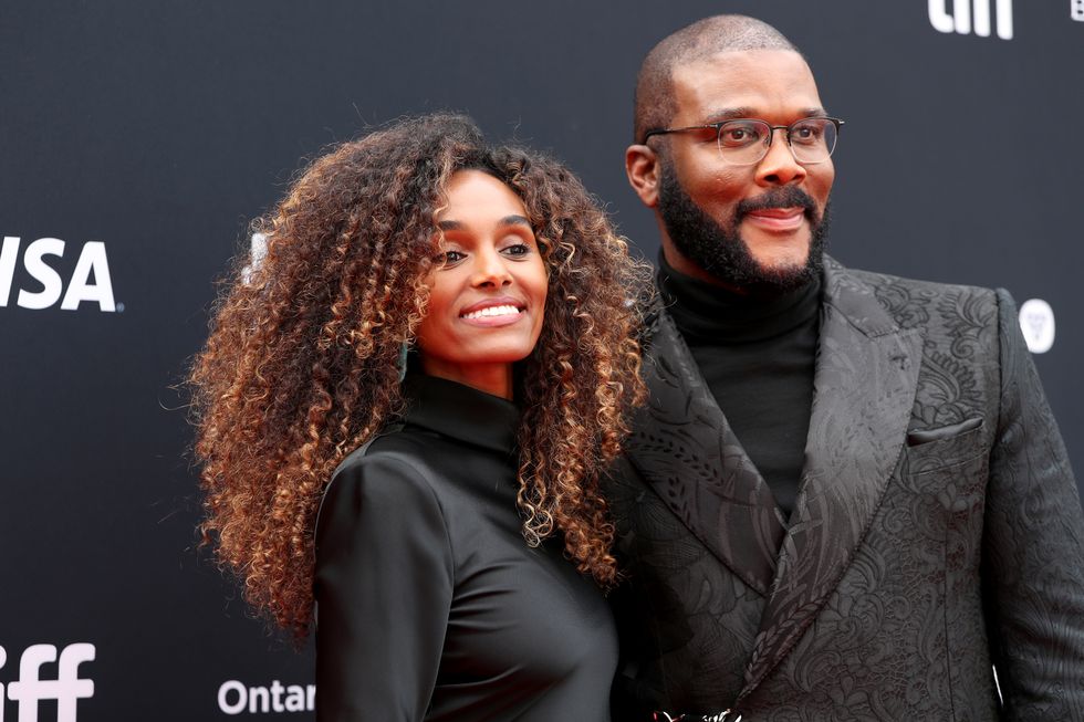 a woman and a man stand together and smile for photos, both wear black outfits