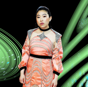 awkwafina in an orange dress surrounded by green swirls