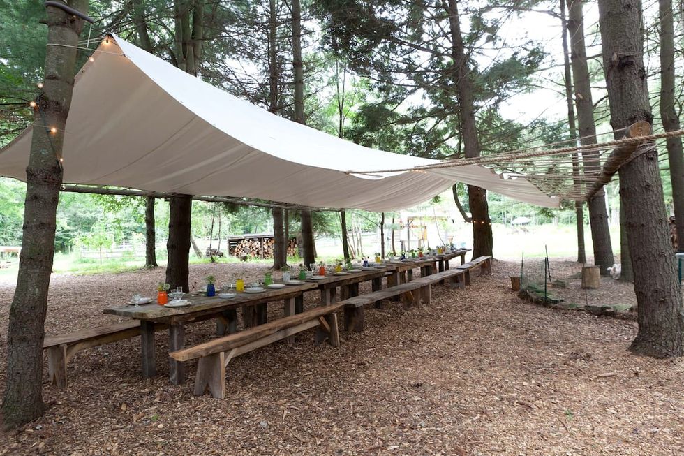dining area with stretch of wooden tables and benches, tented with tarp like material attached to trees lining the dining area