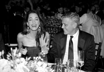 een lachende amal clooney en george clooney tijdens een etentje waar george haar verlovingsring laat zien