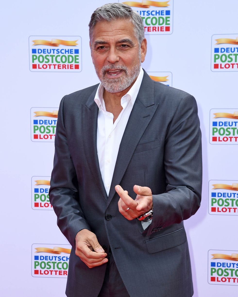 george clooney talking to photographers off camera as he poses on the red carpet