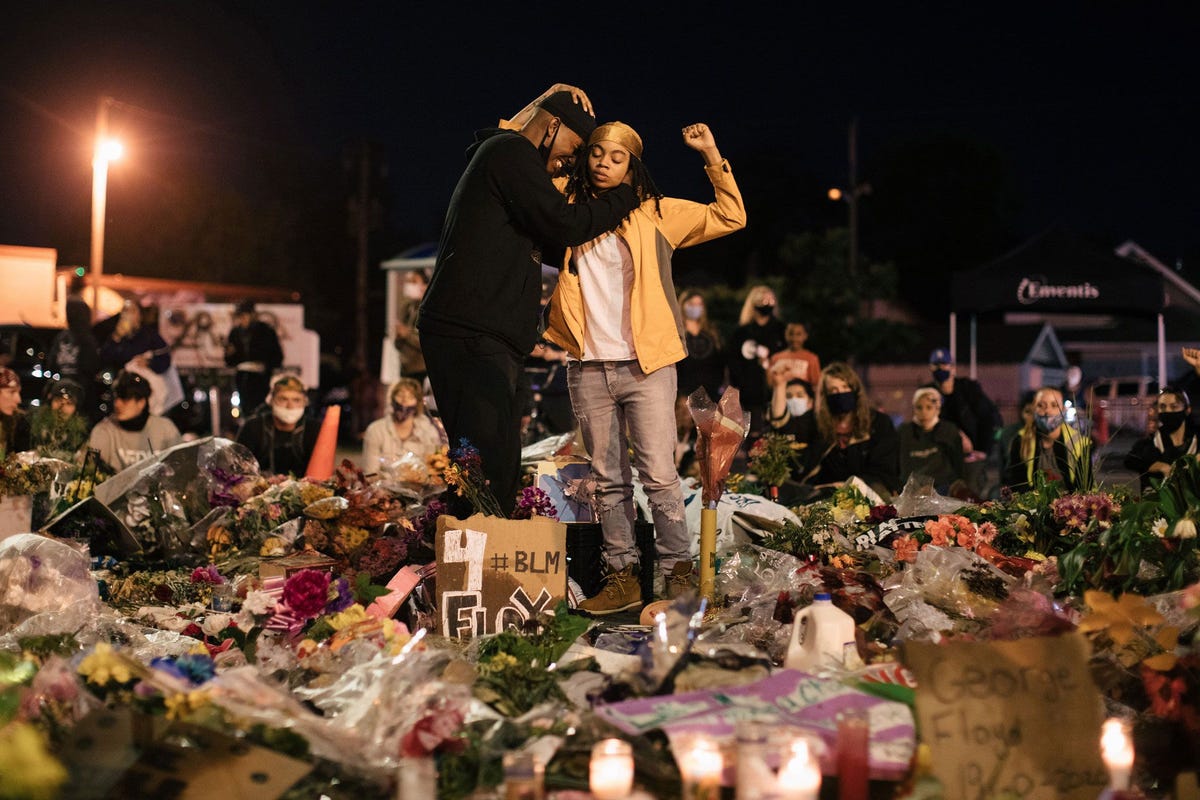 Een vrouw heft de gebalde vuist terwijl ze een man troost op de plek in Minneapolis waar George Floyd in handen van de politie werd gedood Het gebaar is een symbool geworden van weerbaarheid en kracht aldus een activist