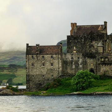 a stone building on a hill by a body of water with urquhart castle in the background