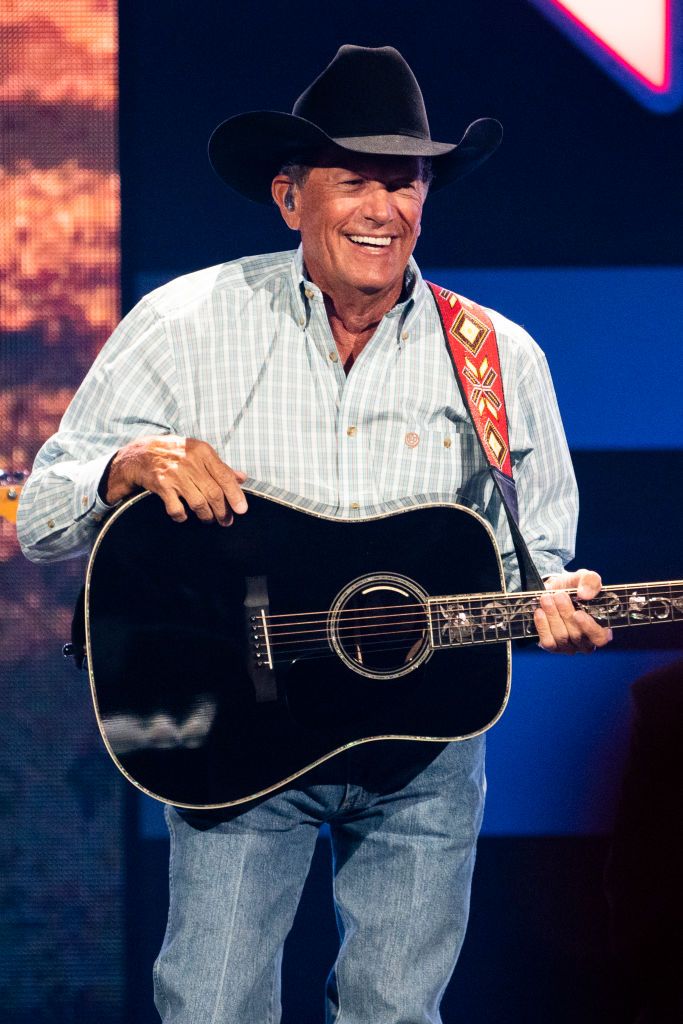 george strait smiling and wearing a cowboy hat while holding a guitar during a performance