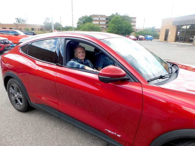 george chartier posing in front of a red mustang mache ev