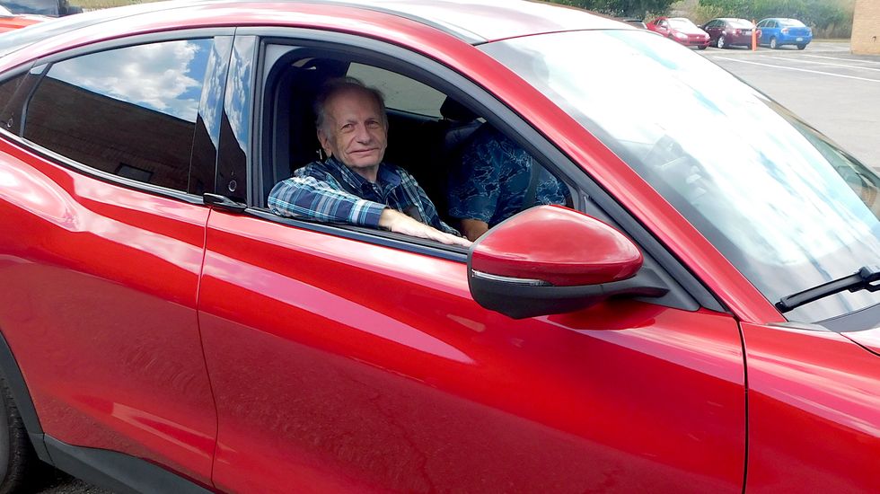 george chartier posing in front of a red mustang mache ev