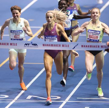 a group of runners leaning toward a finish line tape