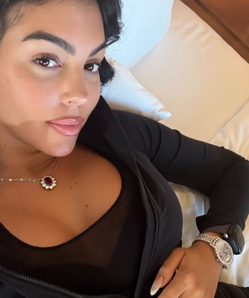 a person reclining on a bed wearing a black top and jewelry