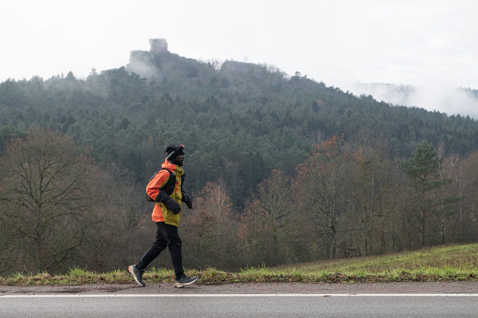 person jogging along a roadside with a mountainous forest in the background