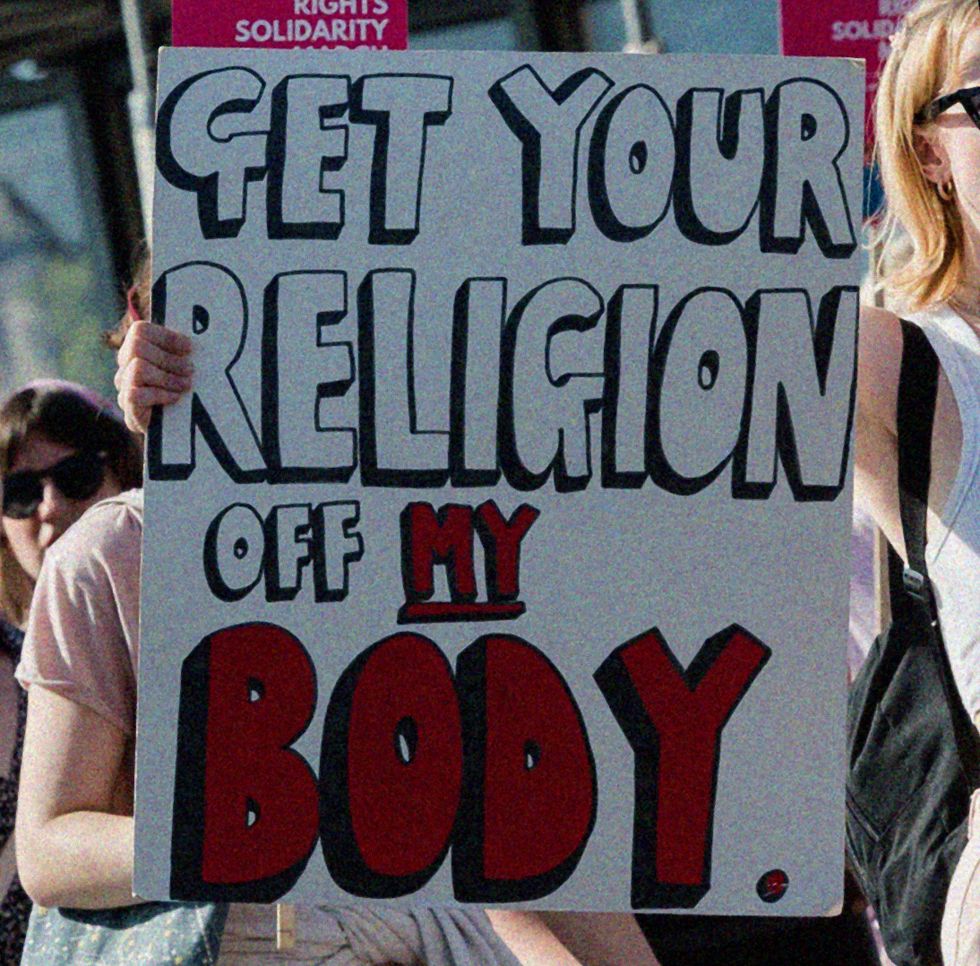 a woman holding a sign saying get your religion off my body