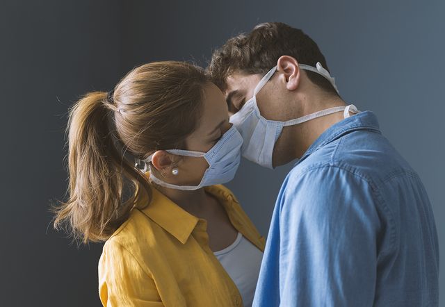 young millennials couple wearing protective face masks and kissing each other, virus spread prevention and people concept