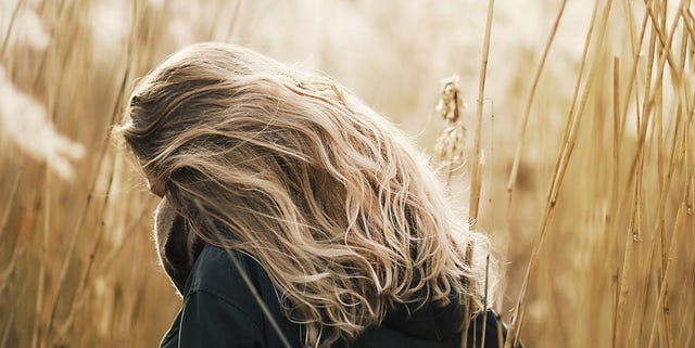 Rear View Of Woman With Blond Hair Standing Amidst Dry Plants On Field