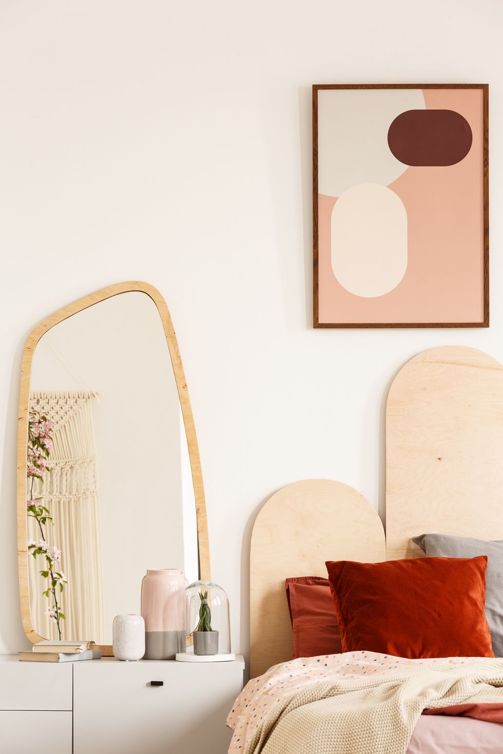 mirror on white cabinet next to bed with red cushions under poster in pastel bedroom interior real photo