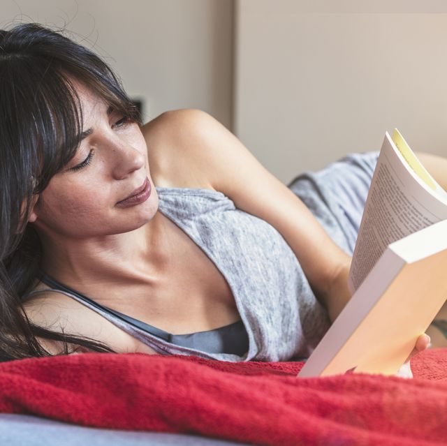 young woman reading book on bed at home