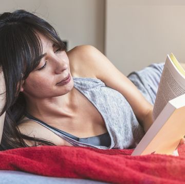 young woman reading book on bed at home