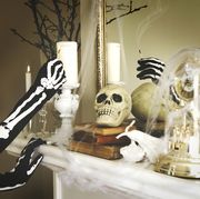 person dressed in a skeleton costume lights a candles halloween composition on fireplace