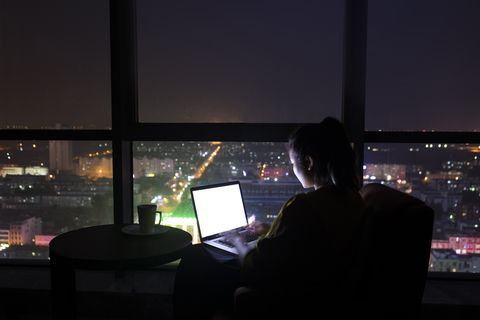 Woman using laptop at night by large windows