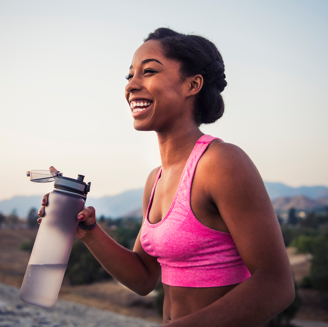 happy female runner in pink sports bra holding water bottle smiling