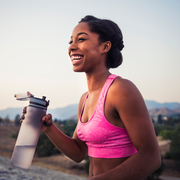 happy female runner in pink sports bra holding water bottle smiling