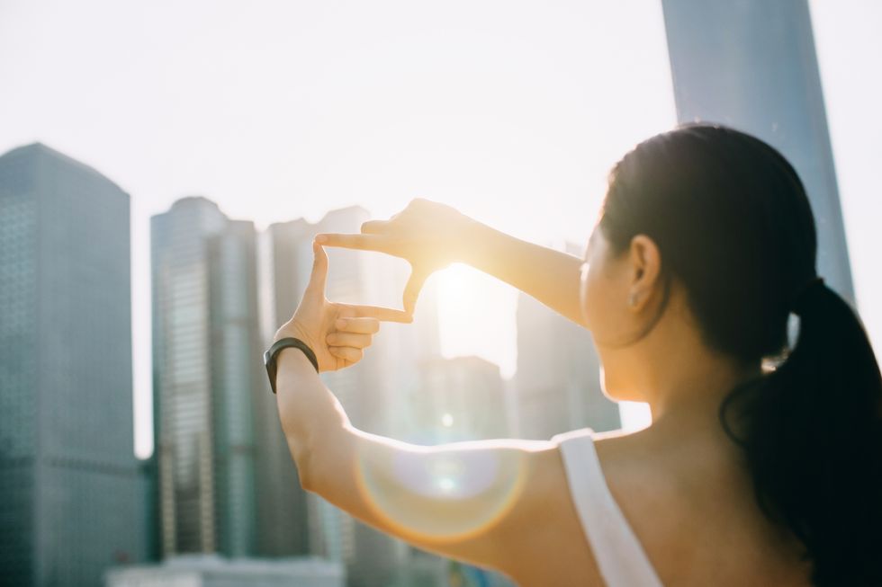 rear view of young woman frames the hong kong city skyline into a finger frame under a sunny sky