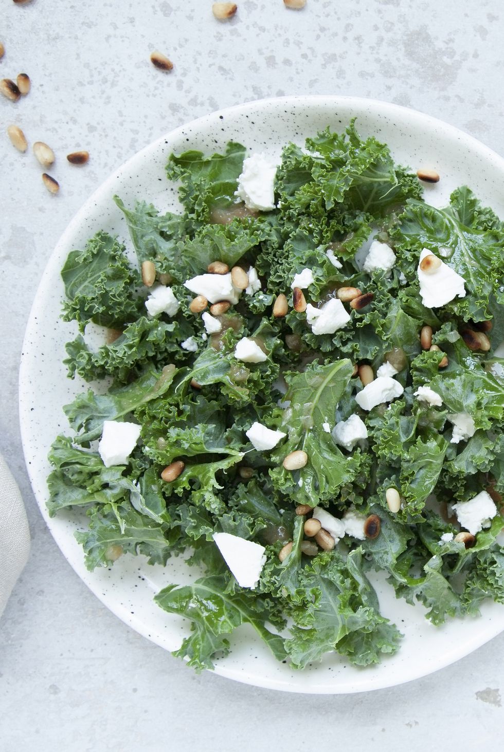 fresh kale salad with goat cheese, pine nuts and sweet balsamic vinegar dressing with onion on grey background